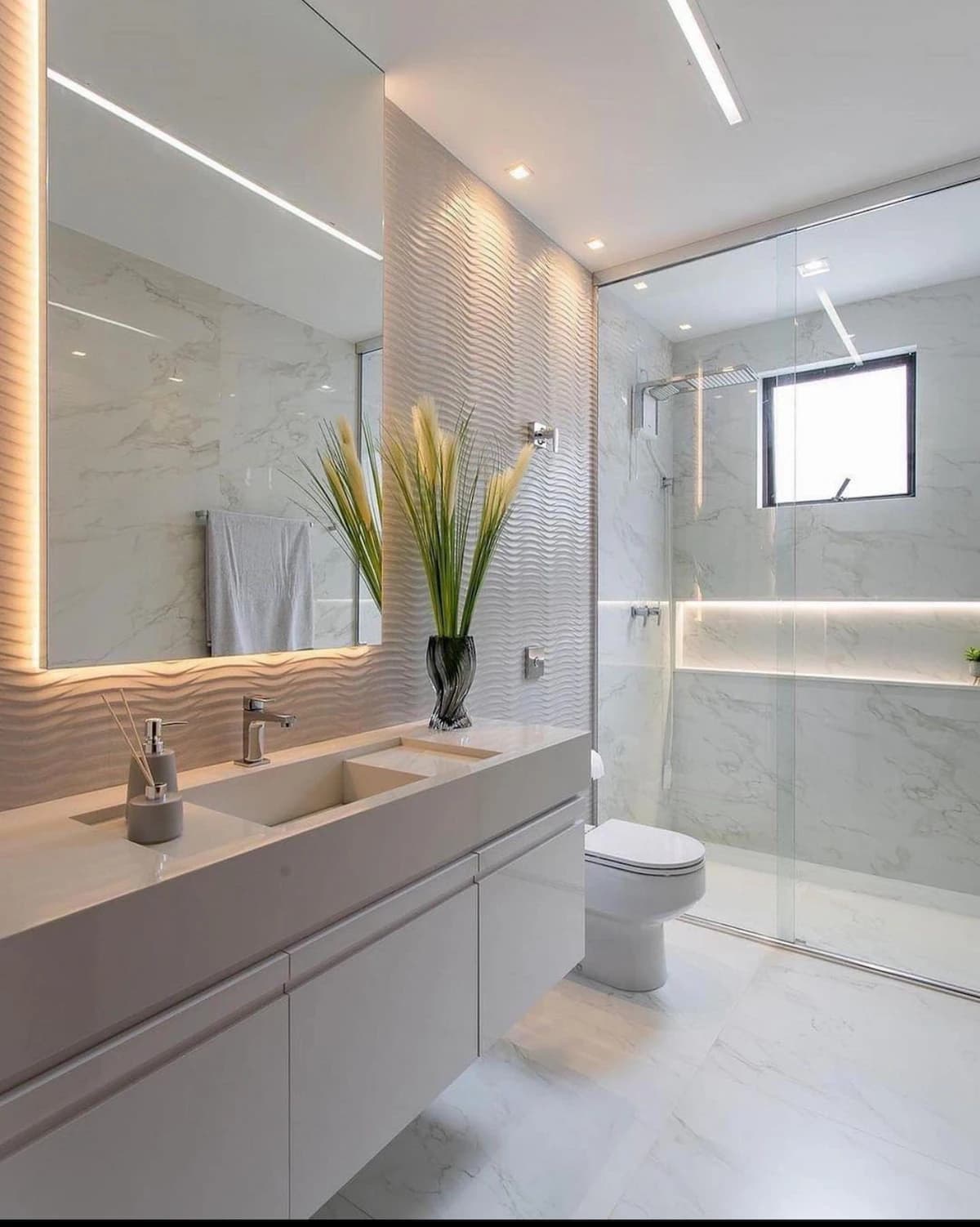 Modern bathroom remodel by IAS Boutique Remodeling in Houston with a floating vanity, backlit mirror, and glass-enclosed shower.