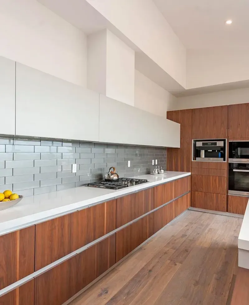 Walnut wood-slab kitchen cabinets with white quartz countertops, a gray glass-tile backsplash, a gas cooktop, and integrated stainless wall ovens.