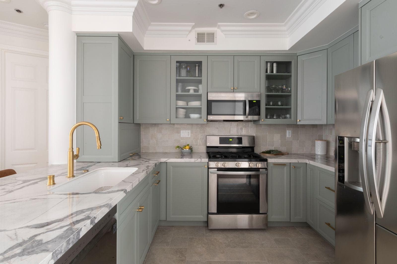 Sage-green kitchen with white marble counters and a gold faucet, remodeled by IAS Boutique Remodeling in Houston.