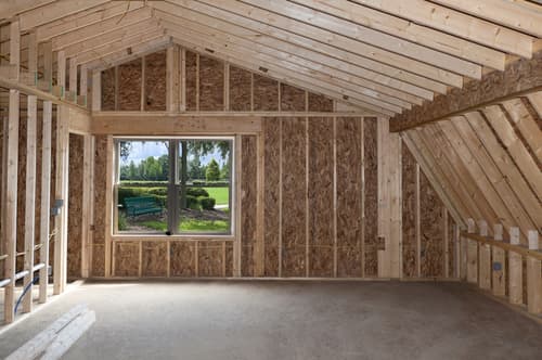 Interior of a home framed down to the studs during a whole-home renovation, with exposed wood wall framing, vaulted roof rafters, and a window overlooking the yard.