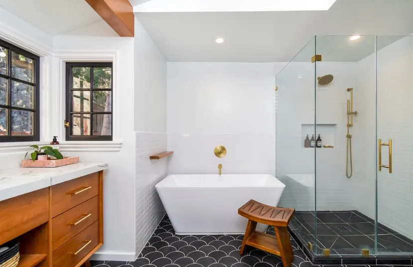 Bathroom with a walnut floating vanity and white marble counter, a freestanding tub with a gold wall-mount filler, a black scalloped-tile floor, and a frameless glass walk-in shower with gold fixtures.